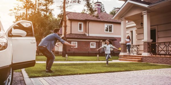 Happy family. Dad came home, daughter is running to meet him while wife is waiting on the house's porch.