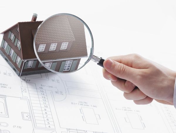 Concept image of a home inspection. A male hand holds a magnifying glass over a miniature house.