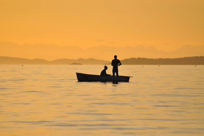 a beach at sunset focus is on a small rowboat with two people in it