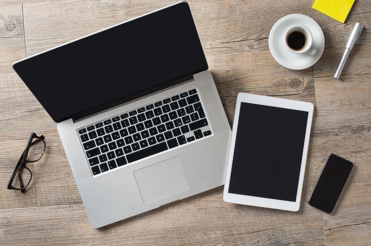 reading glasses next to a laptop, tablet and smartphone on a table