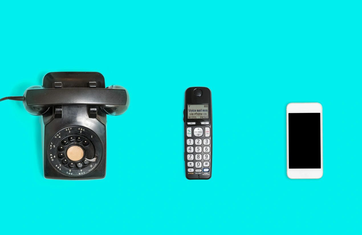 a blue background with three phone, a rotary phone, feature phone and smart phone