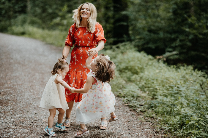 Mother playing with two young daughters outdoors.
