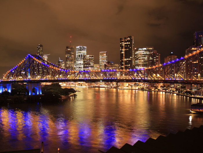 night view of Brisbane's Story Bridge illuminated in vibrant colors reflected on the river.